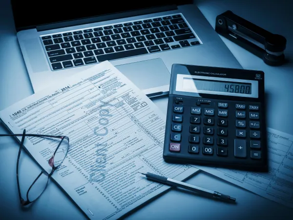 A laptop on a glass table displaying financial charts and data dashboards, including bar graphs, line charts, and key performance metrics.